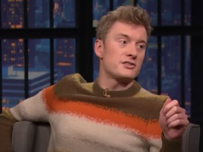James Acaster is wearing a sweater which has brown, orange, and peach color mixed.